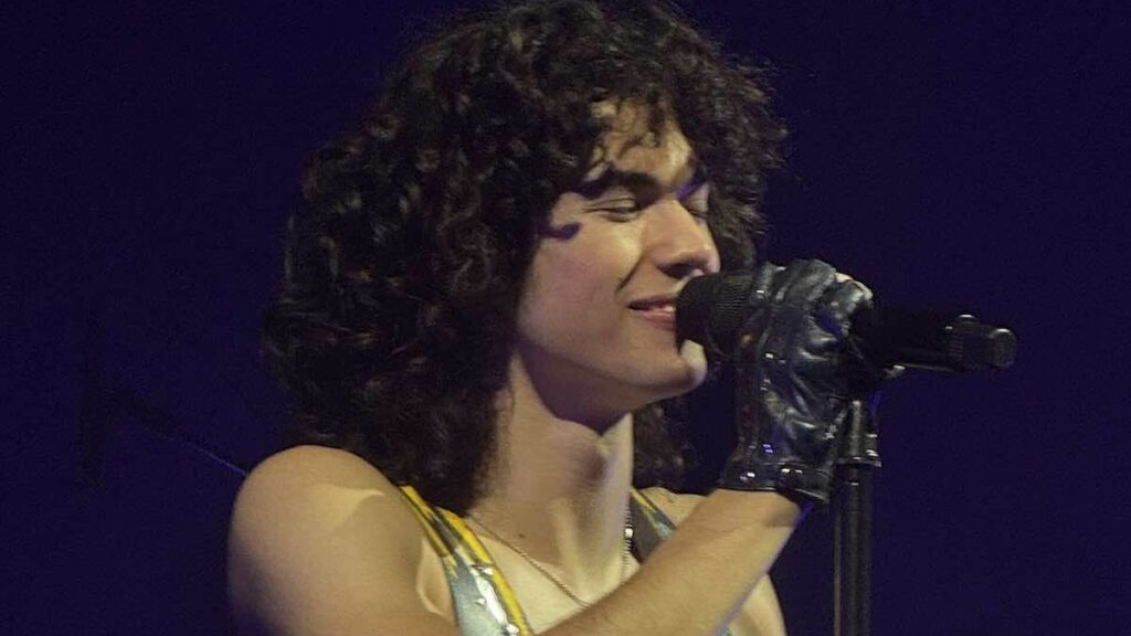 Conan Gray biography portrait — young man with curly hair wearing a white jacket.