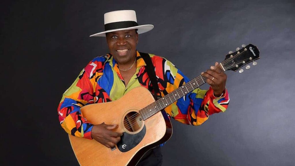 Afric Simone biography portrait — smiling and posing for a photo.