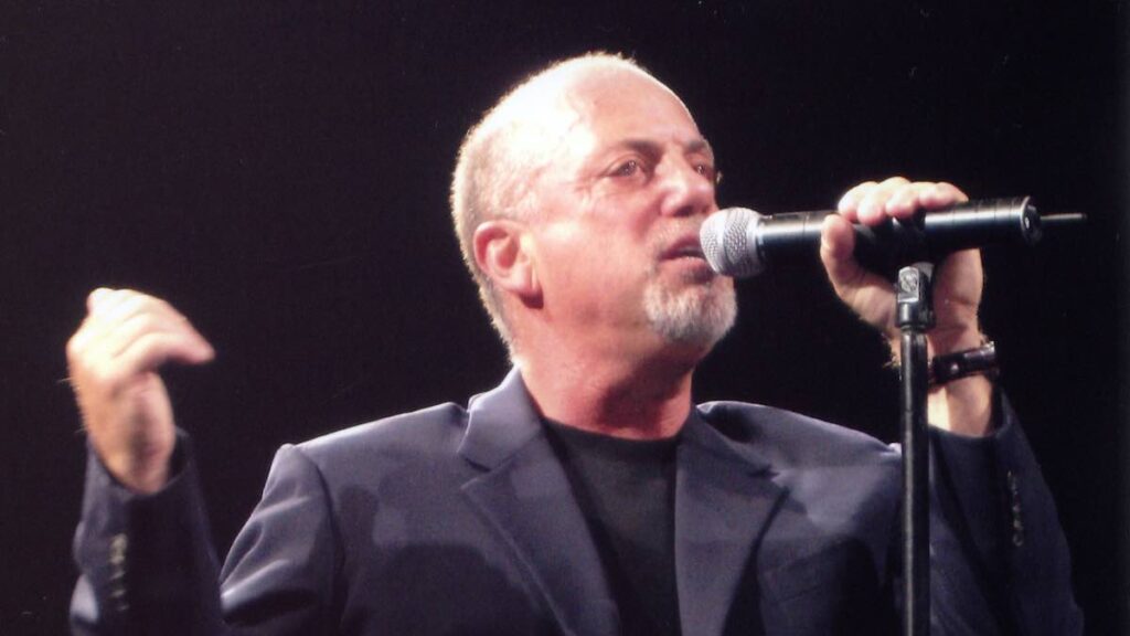 Billy Joel biography portrait — performing live on stage playing the piano during a concert in Perth.
