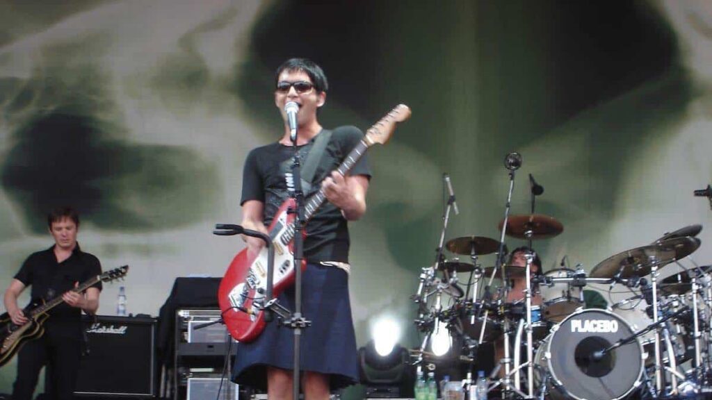 Brian Molko biography portrait — performing on stage in a skirt.