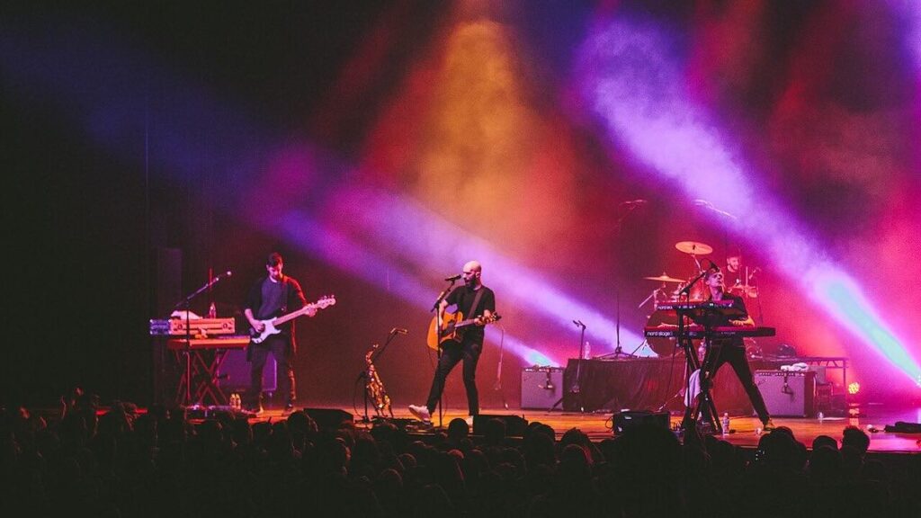 X Ambassadors biography portrait — performing live on stage during a concert in 2015.